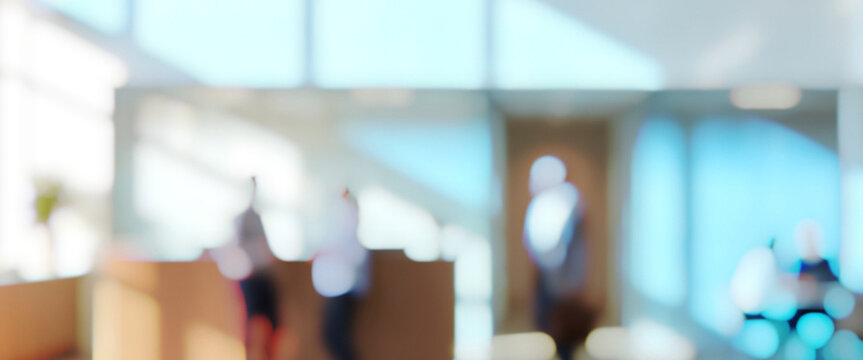 A blurred office interior with sunlight streaming through windows, creating a bright atmosphere. People can be seen in the background, engaging in conversation.