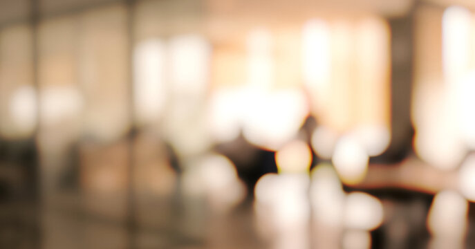 A blurred interior view of an office space, showcasing people engaged in discussions and collaboration. Soft lighting enhances the ambient atmosphere.
