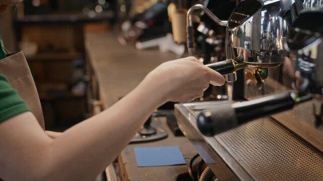 Young adult barista tamping ground coffee into portafilter, attaching it to espresso machine, starting extraction. Perfect for cafe branding and coffee business marketing