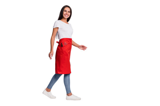 Full size photo of young happy cheerful lovely woman hairdresser go walk in red apron isolated on grey color background
