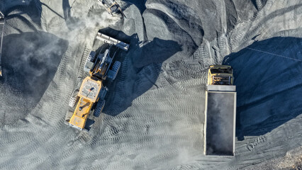 Aerial view of heavy equipment loading gray stone material into a dump truck at a mine site © A Denny Syahputra