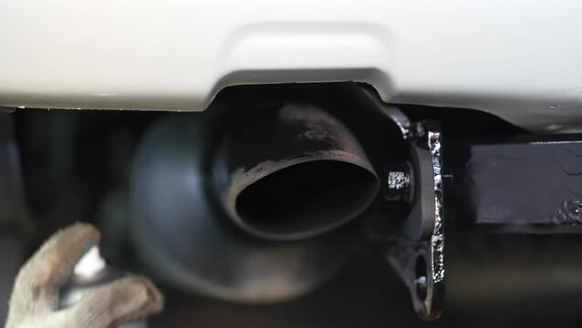 Man spraying black protective aerosol coating onto car exhaust tailpipe.