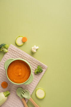 Baby's first feeding with healthy vegetable puree in a silicone bowl and spork on light green background