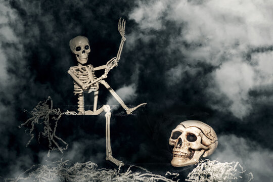 Halloween time. A skeleton crawling out of a tomb, a skull, a clock on a black, smoky, dusty background