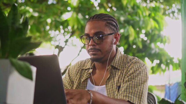 Focused freelancer with eyeglasses working on laptop outdoors