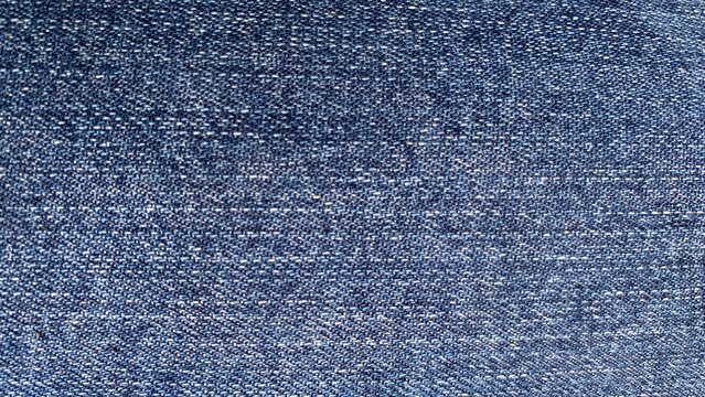 Macro close-up of blue denim fabric highlighting diagonal twill weave texture and fine textile stitching details