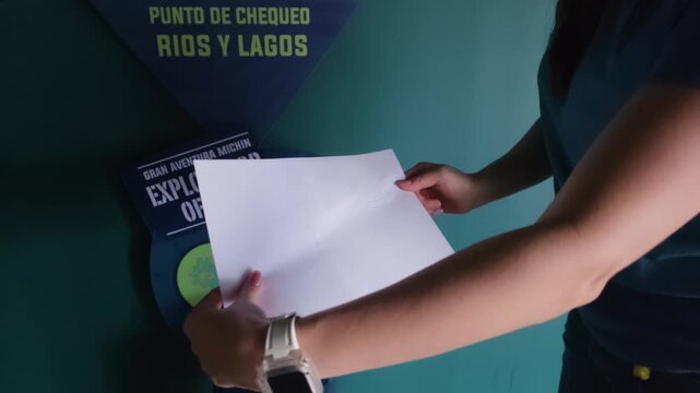 A young Latina woman demonstrates an embossed seal featuring an otter and river design, obtained from a press at a 'R&iacute;os y Lagos' exhibit at Acuario Michin.