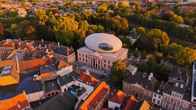 Golden-hour aerial of Museum de Fundatie in Zwolle, Netherlands, highlighting its distinctive oval rooftop extension above historic red-roofed streets and leafy city center.
