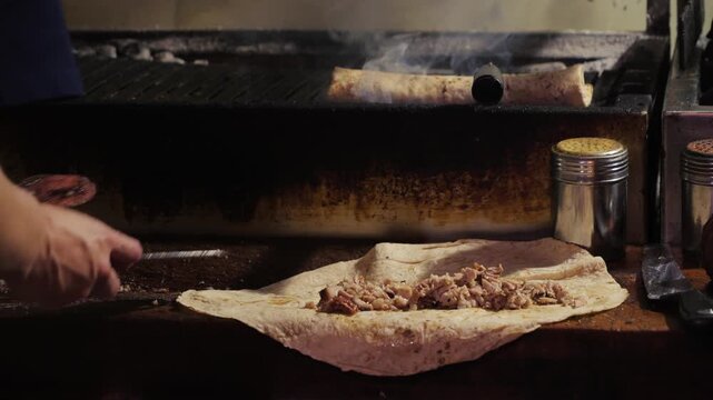 Preparing traditional Turkish kokorec by placing finely chopped grilled lamb intestines onto flatbread. Street food preparation with a cook assembling a savory wrap. High quality 4k footage