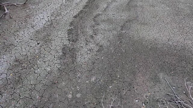 A smooth forward camera push moves low over a cracked dried soil ground surface with scattered dry roots and twigs, capturing arid earth patterns on a lake bed in Als&oacute;mocsol&aacute;d, Hungary, Europe.