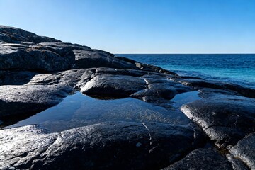 Fototapeta premium Rocky shoreline with tide pools reflecting clear blue sky and ocean