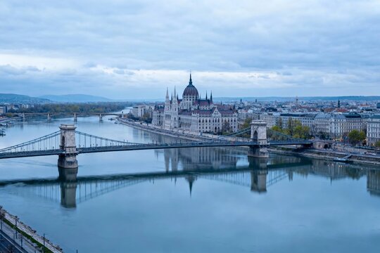 View of a historic parliament building and suspension bridge over a calm river in a European city