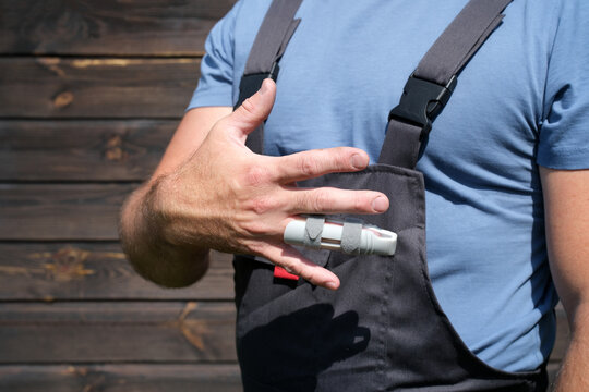 Worker in protective workwear showing injured finger with splint after workplace accident, hand injury and safety concept