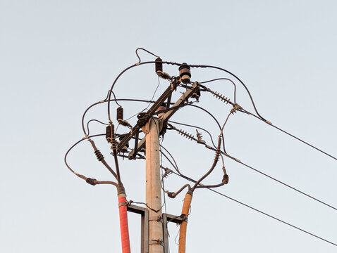 High-angle view of a concrete utility pole with complex electrical wires, lines, and insulators against a clear bright sky.