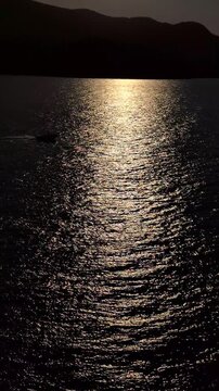 Sunlight glimmers on the gently rippling waters of the bay, reflecting the sunset as a motorboat passes by.