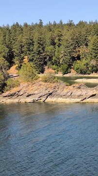 Rocky shores of islands and peninsulas with trees and evergreens in Burrard Inlet on a sunny summer day. Beautiful nature in British Columbia, Canada.