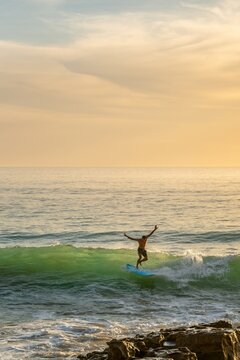 Man with arms wide open surfing a wave at sunset