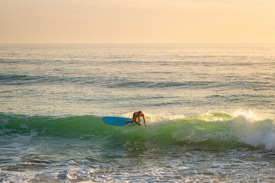 Surfer riding a blue surfboard on a breaking wave under a golden sky