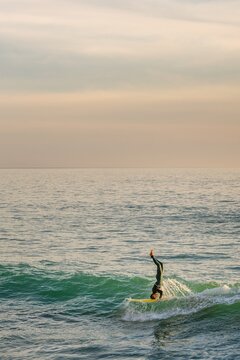 Surfer balancing on headstand while riding a wave at sunset