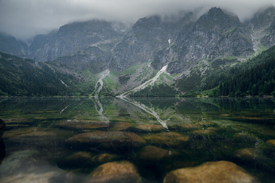 Morskie Oko lake reflects misty Tatra mountains and green forest