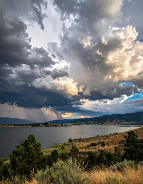 Dramatic storm clouds gather over a serene lake and rolling hills.