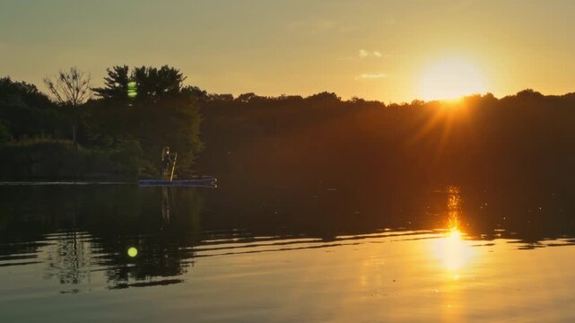 A young woman and her Belgian Malinois dog paddleboarding on a calm Ukrainian lake with a picturesque forest shoreline during a golden hour sunset.