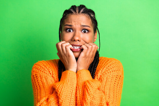 Young woman in bright orange knit sweater shows anxious expression while posing against a vivid green background for versatile stock photo