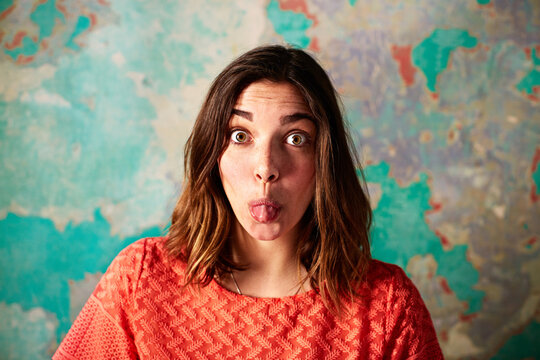 Portrait, woman or tongue out with goofy expression on peeling or damaged wall in abandoned house. Funny face, female person or humor with shocked eyes or reaction in weathered background or building