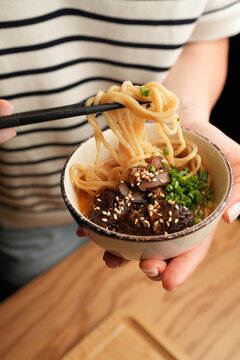 Woman holding Asian ramen noodle bowl with chopsticks close up
