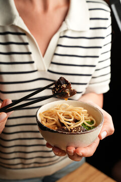 Woman holding Asian ramen noodle bowl with chopsticks close up