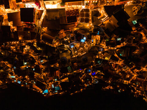 Overhead 90 degree aerial drone shot of Oia village resort roofs and lit pathways at night, Santorini, Greece