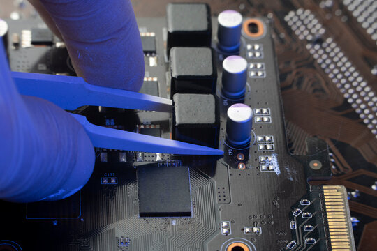 Macro view of technician using precision tweezers to place power inductor on data server hardware circuit board.