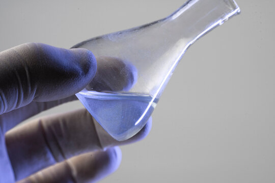 Scientist holding glass conical flask with blue chemical solution for pharmaceutical or cosmetic laboratory testing
