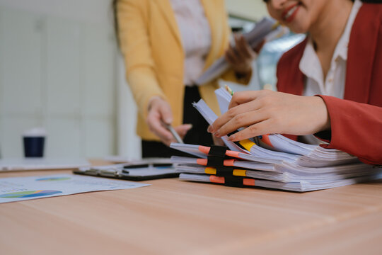 Businesswomen reviewing organized documents and reports at an office desk, representing teamwork, financial analysis, project management, administration, and business planning.