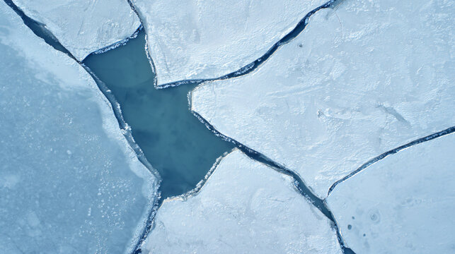 top-down aerial photograph of a partially frozen lake, enormous irregular plates of pale blue ice separated by narrow dark-water cracks, subtle warm sunlight illuminating only a few ice edges