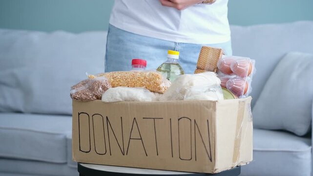 Donation box with food. The volunteer puts the different cereals into a cardboard box.
