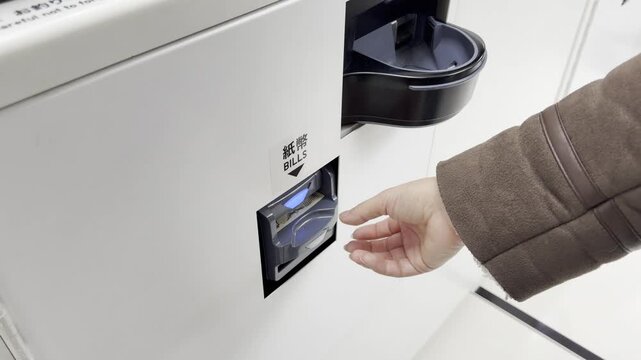 Hand places a 1000 yen banknote into the bill acceptor of a vending machine, showcasing the payment process in a well-lit indoor area