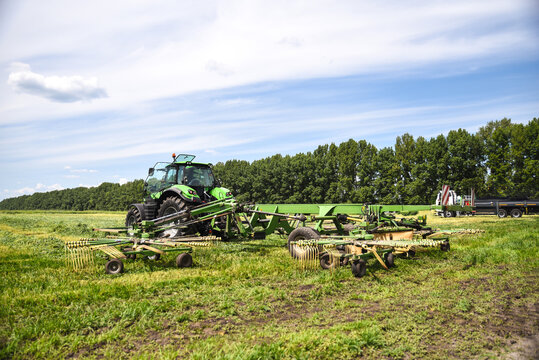 Tractor working with a forage tedder in a field, turning and spreading freshly cut grass to speed up drying during haymaking operations.