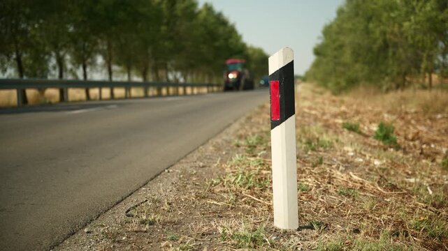 Roadside delineator reflector post on a rural asphalt highway as a tractor approaches. Concept of road safety, traffic marking, rural infrastructure, and agricultural transport. 4K.