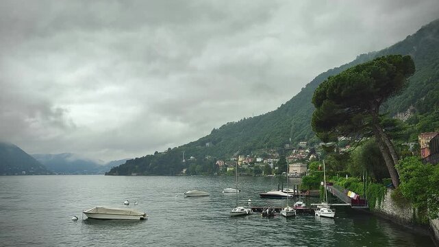 Lake Como, Moltrasio, Italy. Tranquil lake scene with boats floating gently, framed by green mountains and overcast skies after rain