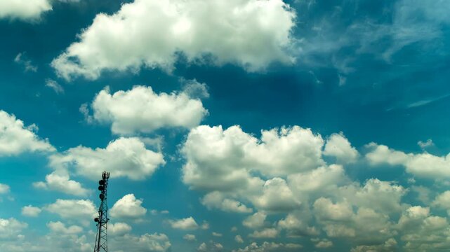 Time-lapse of fluffy white cumulus clouds drifting across a vibrant blue sky with a telecommunications tower in the foreground
