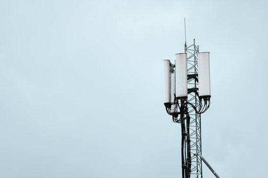 Vertical telecommunications mast with antennas transmitting signals under a cloudy sky