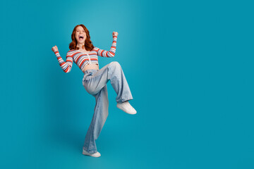 Happy young woman jumping in studio in casual striped crop top and wide jeans, celebrating with...