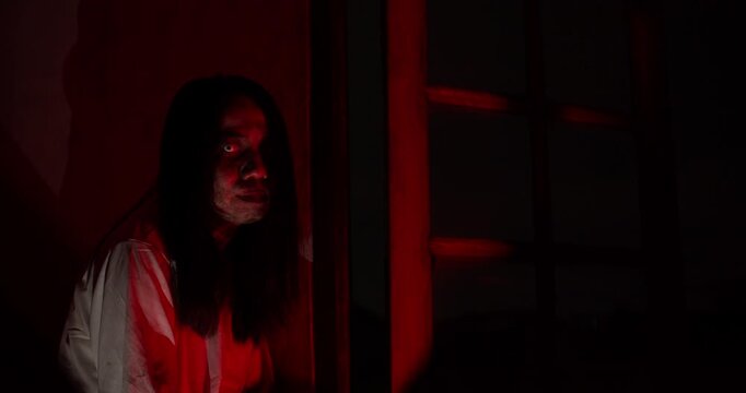 A terrifying ghost with a bloody face lurks in a dark, haunted house, illuminated by sinister red light for a horrifying Halloween scene.