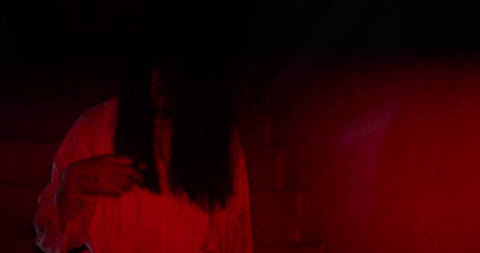 A terrifying ghost woman with a scary disfigured face haunts a dark basement, lit by an ominous red light for a Halloween horror movie scene.