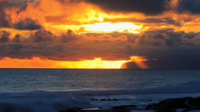 Dramatic Sunset Over Ocean with Golden Light Rays and Rolling Waves at Coastal Cliff