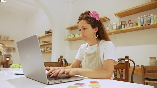Ceramist woman working on laptop in her small business pottery workshop