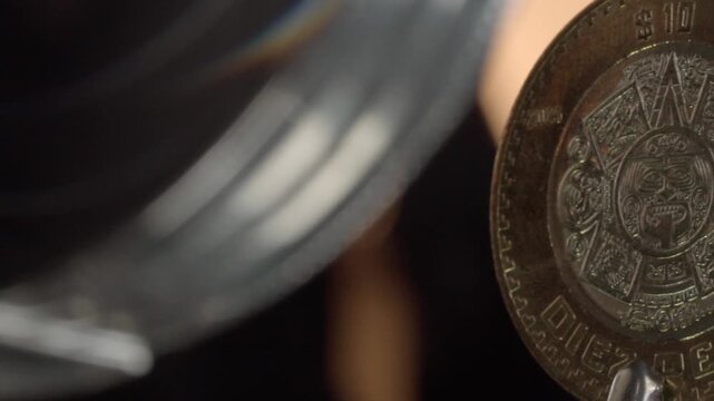 Macro close up of a Mexican coin showing an intricate central emblem, engraved lettering, decorative details, ridged edge, metallic surface, and dark background in Mexico.