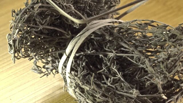 Macro view of dried herb bundles with thin stems and curled leaves arranged on a wooden surface, highlighting their dry texture, natural form, and earthy appearance in Mexico.