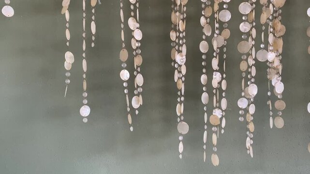 Shell wind chimes swaying gently in the breeze against green wall background. 4K.